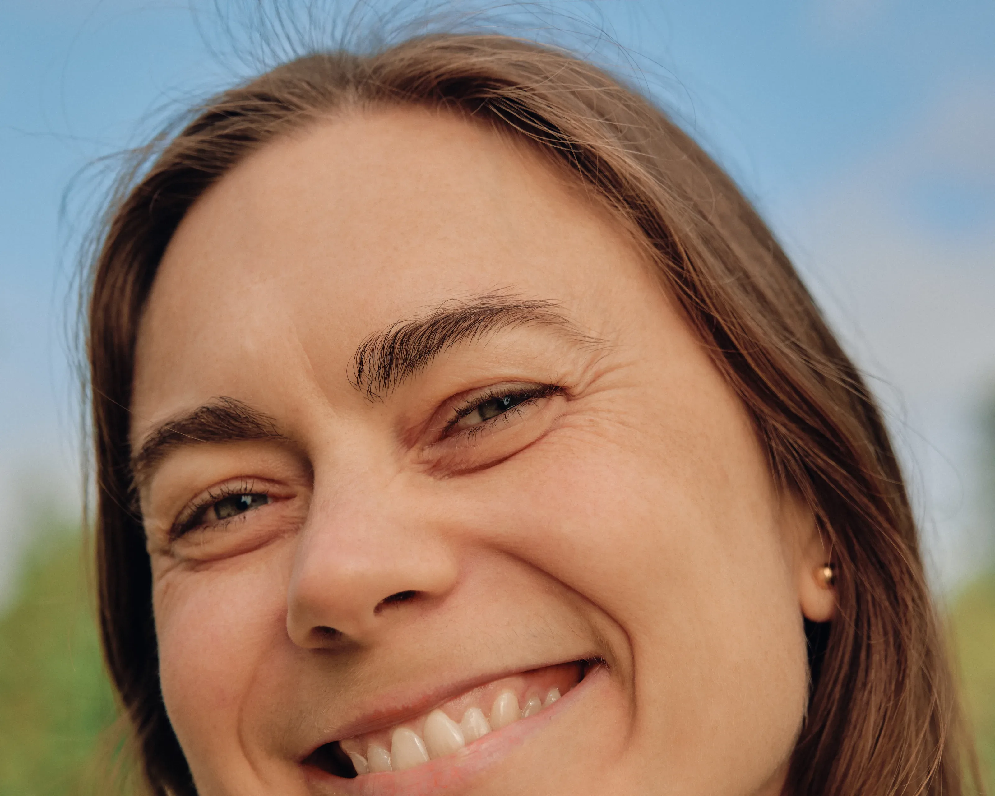 Kvinne smiler i dagslys, nærbilde av øyne og bryn.