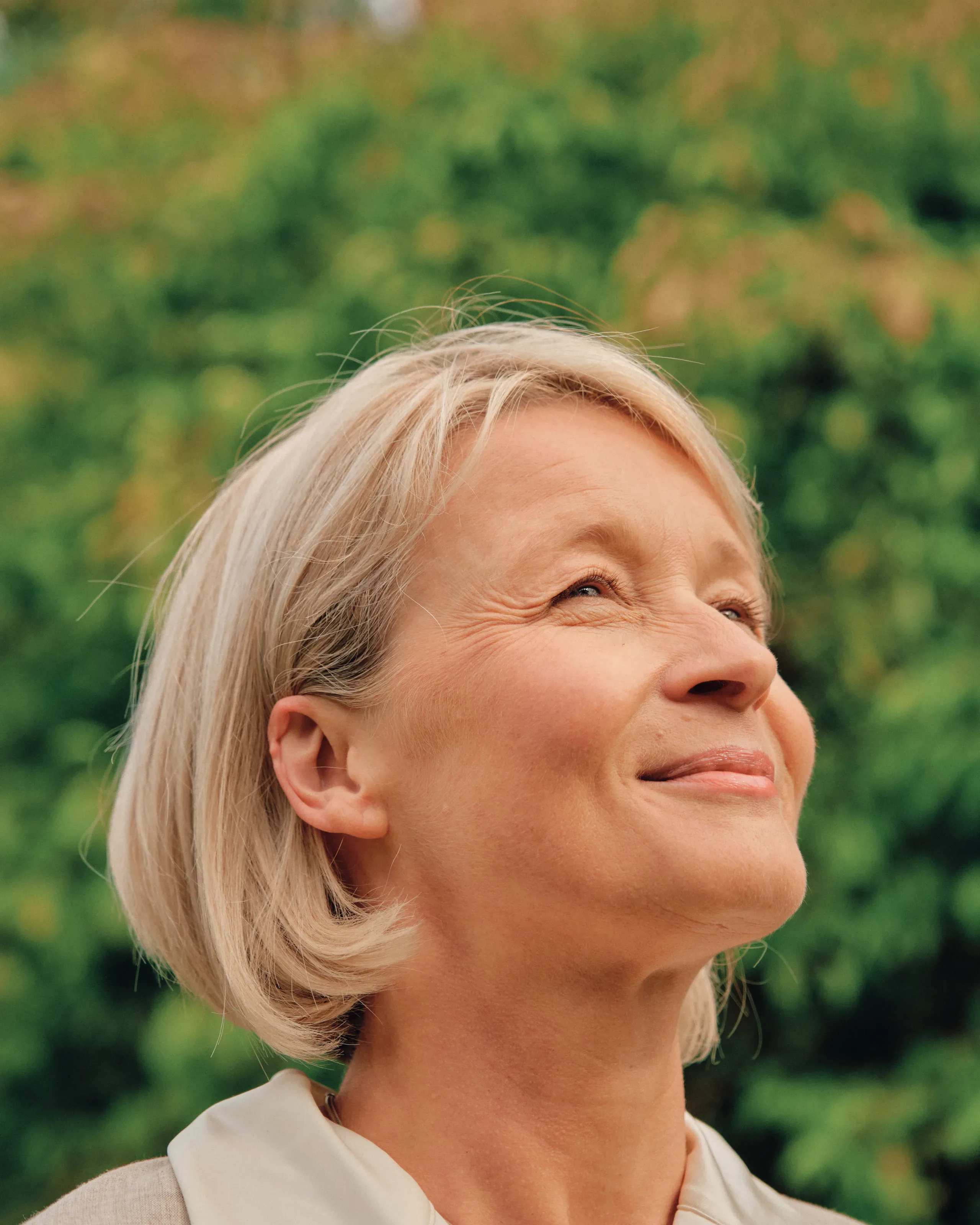 Eldre kvinne smiler i profil utendørs.